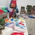 Handknitted plants, jellyfish and octopus arranged on a table. This is part of the Scotia Crafters display in The Devil's Porridge Museum's education room. Some handmade bags are in the background.