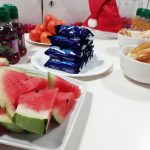 An arrangement of food on a table including watermelon, mini rolls, crisps, fruit shoots and satsumas for The Children's Christmas Party.