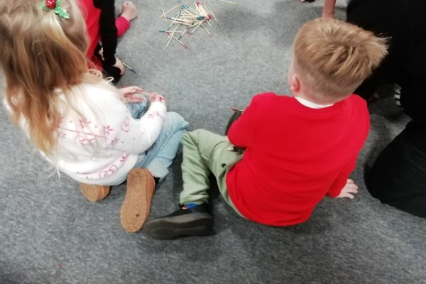 Children's Christmas Party 2025 17 Children sat in a circle playing pick up sticks on the floor.
