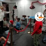Two adults dressed to look like snowmen. Some children are sat and stood around them.