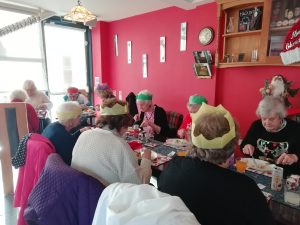 Members of The Devil's Porridge Museum's Cordite Club sat eating Christmas dinner in The Devil's Porridge Museum's Café. They are wearing festive party hats.