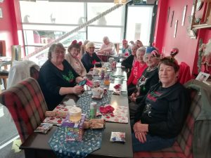The Devil's Porridge Museum's Cordite Club sat around some tables in The Devil's Porridge Museum. They are wearing festive headwear and jumpers.