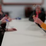 Someone's hand playing with an old fashioned cup-and-ball game next to a table. Some other people are sat around the table in the background.
