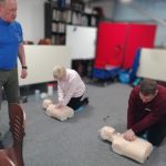 Two members of The Devil's Porridge Museum's team preforming CPR compressions on two models. First Aid instructor Stuart is stood in front of them.