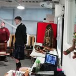 Young volunteer and bagpiper Scott stood in The Devil's Porridge Museum's education room talking. Youth and Community Engagement Officer Tom is in the background.