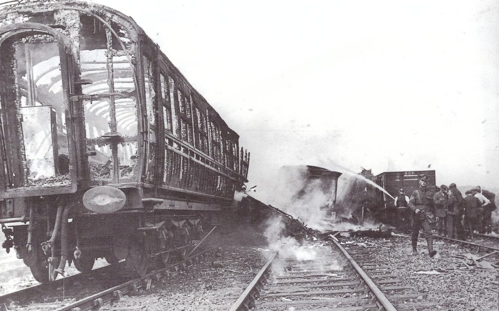 A burnt out train carriage on a railway track with a person hosing it with water. This is a black and white archive photo from the past.