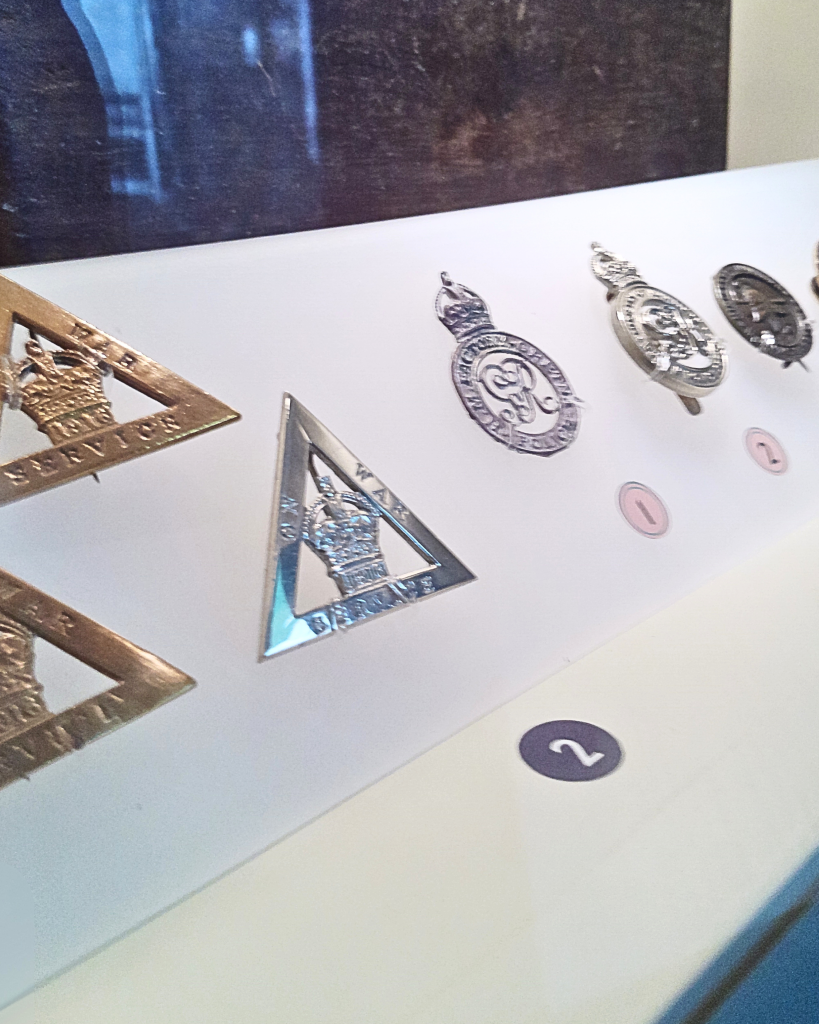 Some triangle On War Service badges and round Women's Police Force Badges for H.M. Factory Gretna on display inside a display case.