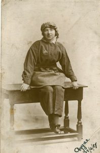 Agnes Renton in her munitions workers uniform sat on a table. This is a black and white photo from the past.