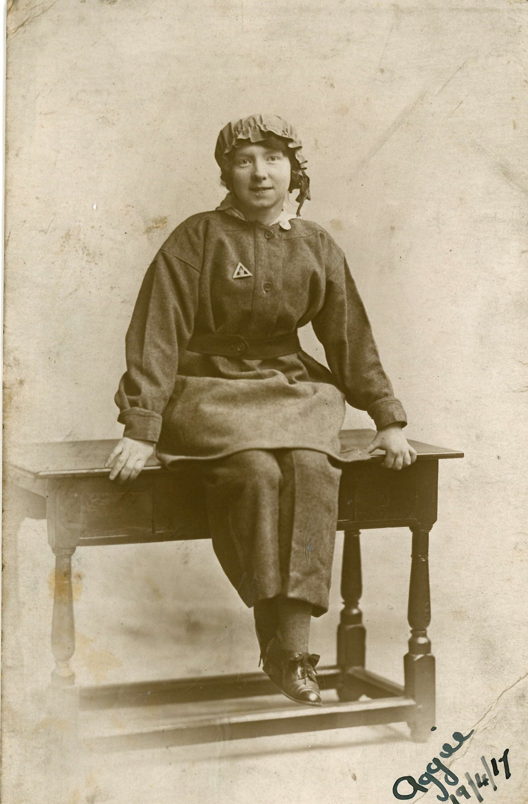 Agnes Renton in her munitions workers uniform sat on a table. This is a black and white photo from the past.