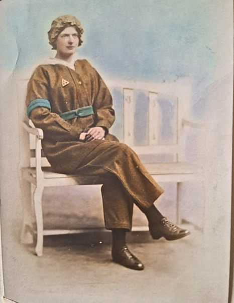 A colourised photo of munitions worker Clara Gladys Bramley Scott sitting on a bench wearing her munitions workers uniform.