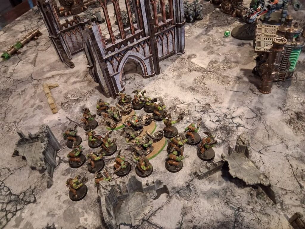 A selection of Warhammer figures and a model of a building arranged on some terrain.